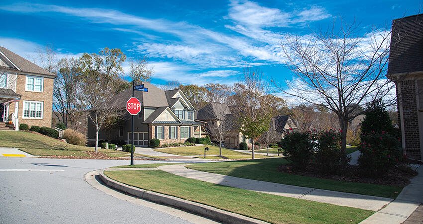 View of a stop sign at a corner in a sunny, tree-lined suburban neigborhood with large houses