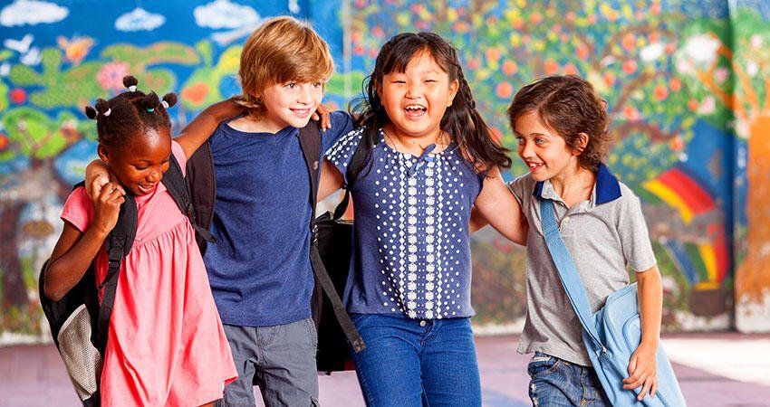 Four elementary school age children hold each other around the shoulders while walking and smiling