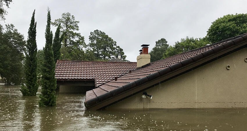 Image of the roof of a house peaking out of flood waters, the rest of the house fully submerged