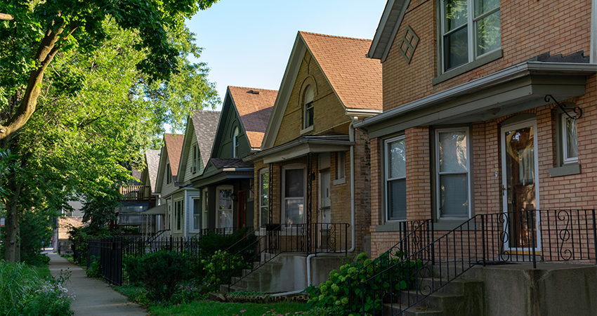 hotograph of an urban residential street showing older multifamily housing with visible exterior wear and maintenance issues