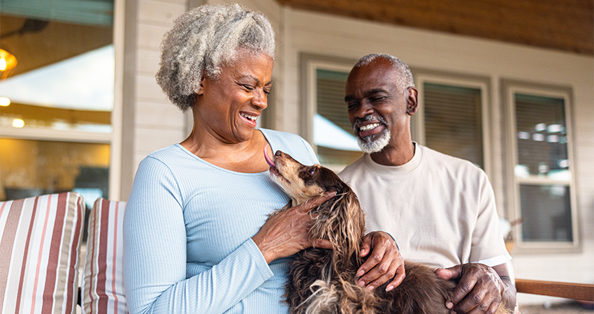 An older Black man and woman sit on a porch holding their dog