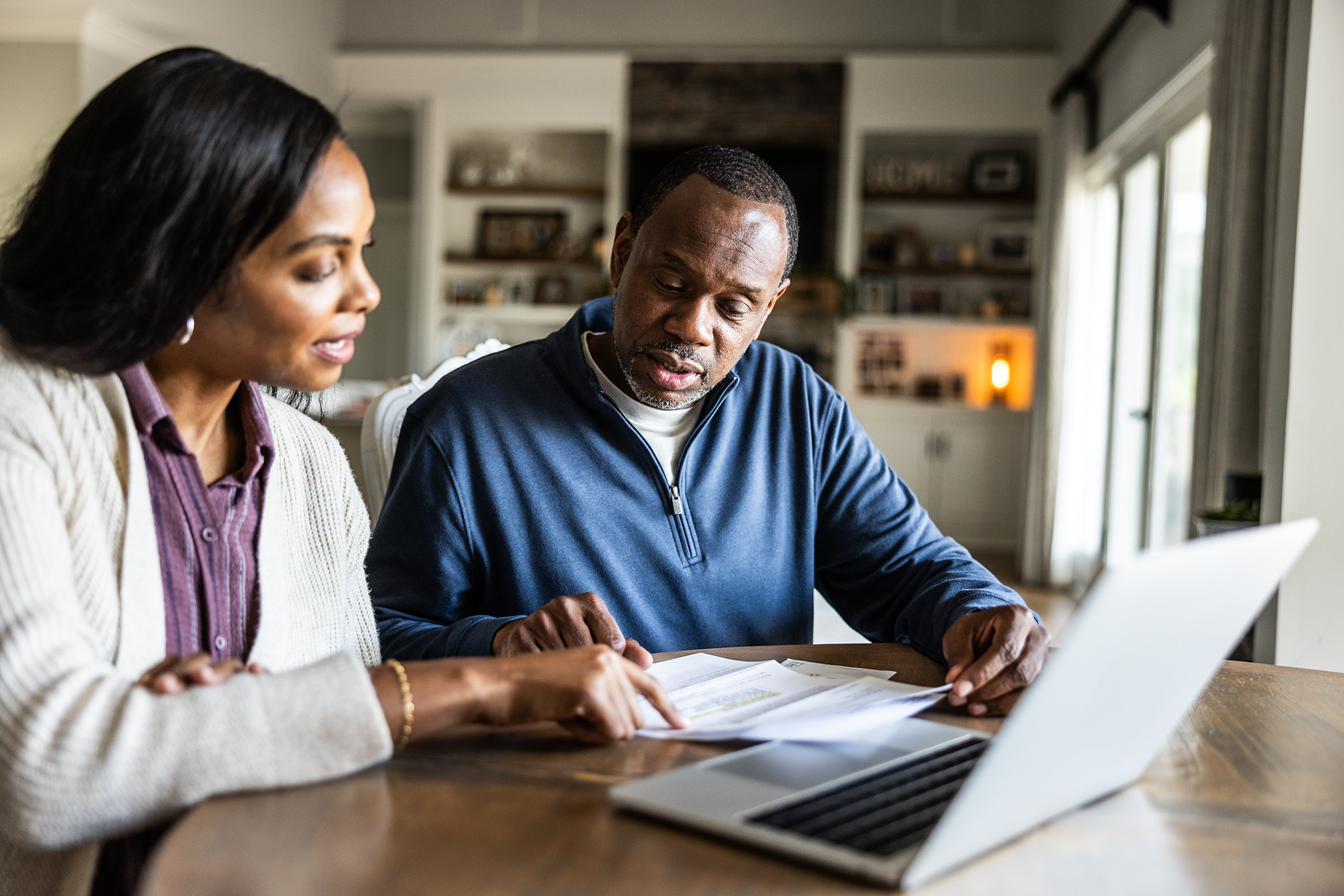 A couple sits at a table looking at paperwork and a laptop