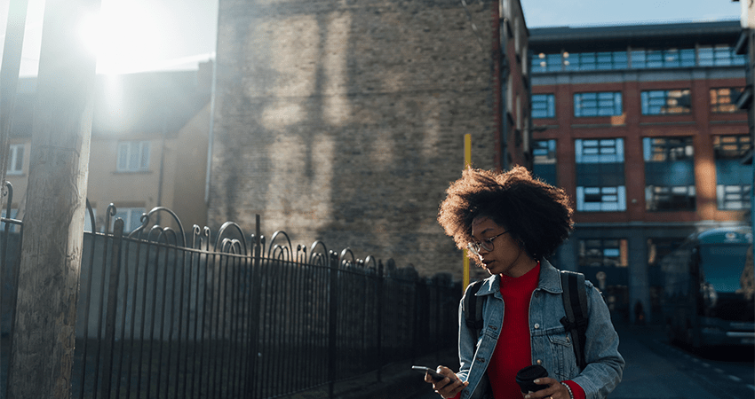 Woman walks down street looking down at phone