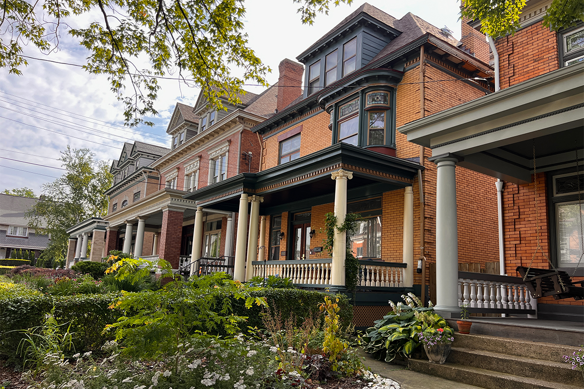 Row of historic brick houses with columned porches and a garden in front.