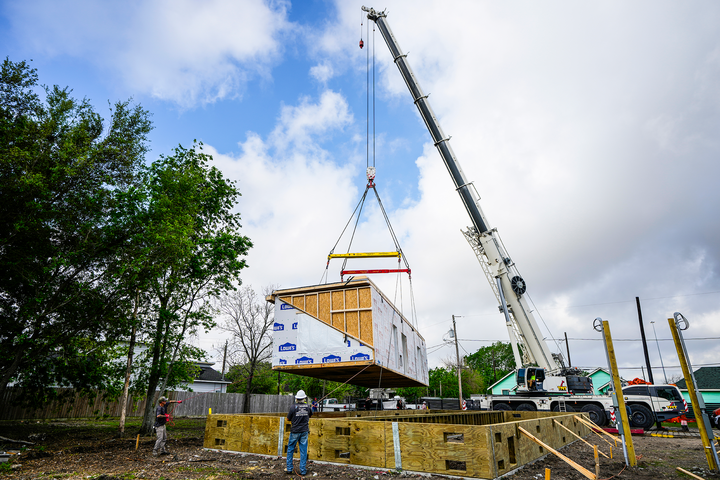 Workers guide a crane‑lifted modular home section onto its foundation at a construction site