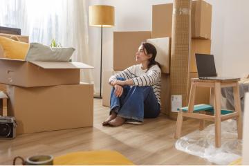 Person sitting among moving boxes in apartment.
