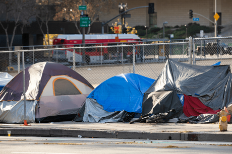 Homeless tents on side of the road in front of a fence