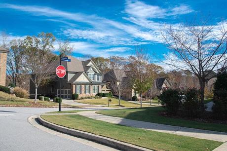 View of a stop sign at a corner in a sunny, tree-lined suburban neigborhood with large houses