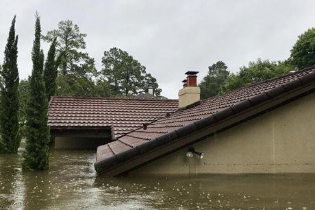 Image of the roof of a house peaking out of flood waters, the rest of the house fully submerged