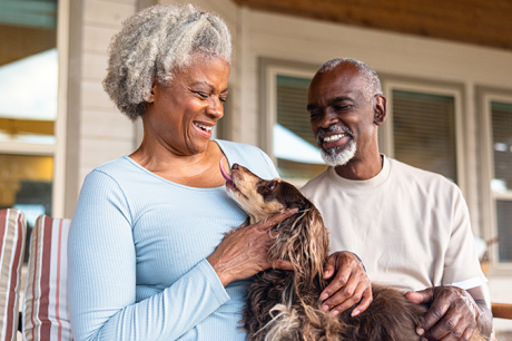 An older Black man and woman sit on a porch holding their dog