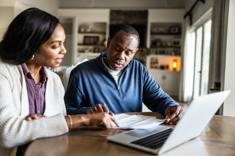A couple sits at a table looking at paperwork and a laptop