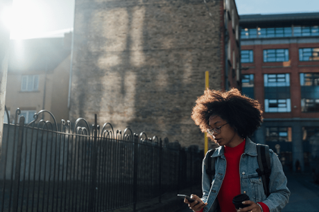 Woman walks down street looking down at phone
