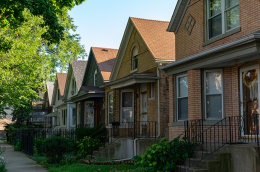 hotograph of an urban residential street showing older multifamily housing with visible exterior wear and maintenance issues
